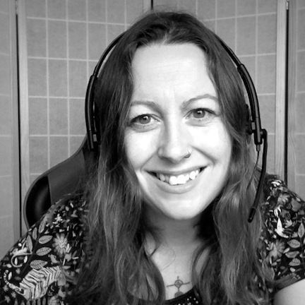 Black and white screengrab of me, a white woman with long hair, sitting in front of a screen, wearing a headset.